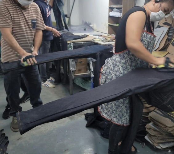 Workers manually sanding and finishing denim jeans in a workshop.