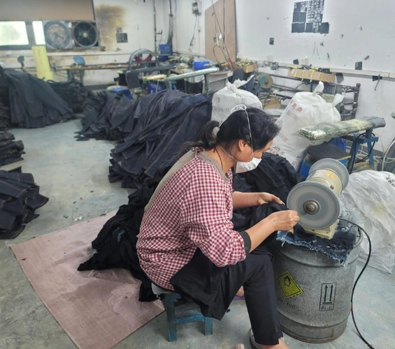 Worker using a bench grinder to finish denim fabric by hand.