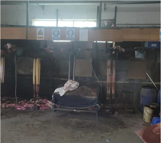 Industrial workshop with materials hanging for treatment and safety signage.