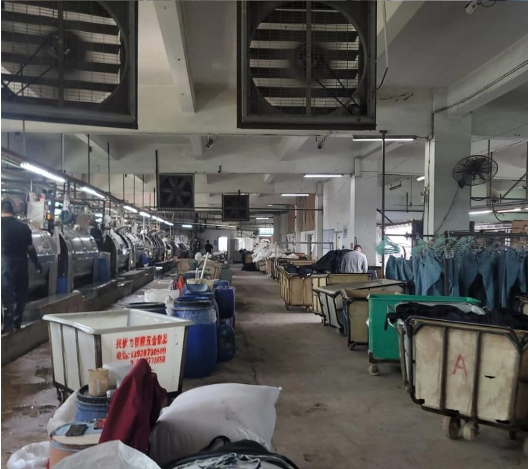 Industrial garment washing facility with machines, carts, and hanging denim.