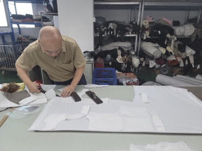 A craftsman precisely cutting garment patterns from white fabric in a textile workshop.